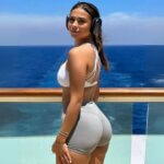 Sophie Rain Turns 21, standing on a balcony in headphones and a white crop top.