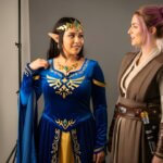 Two women in costume: one as a blue-clad fantasy best cosplay OnlyFans character with gem accents and the other in a brown Jedi-like outfit, posed in a studio setting.